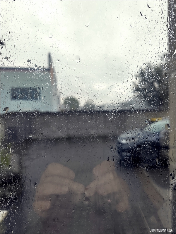 Verschwommener Blick durch ein Fenster, an dem Regen hinunter läuft, auf einen Parkplatz. Für die Aktion Zwölf von Zwölf im Juli