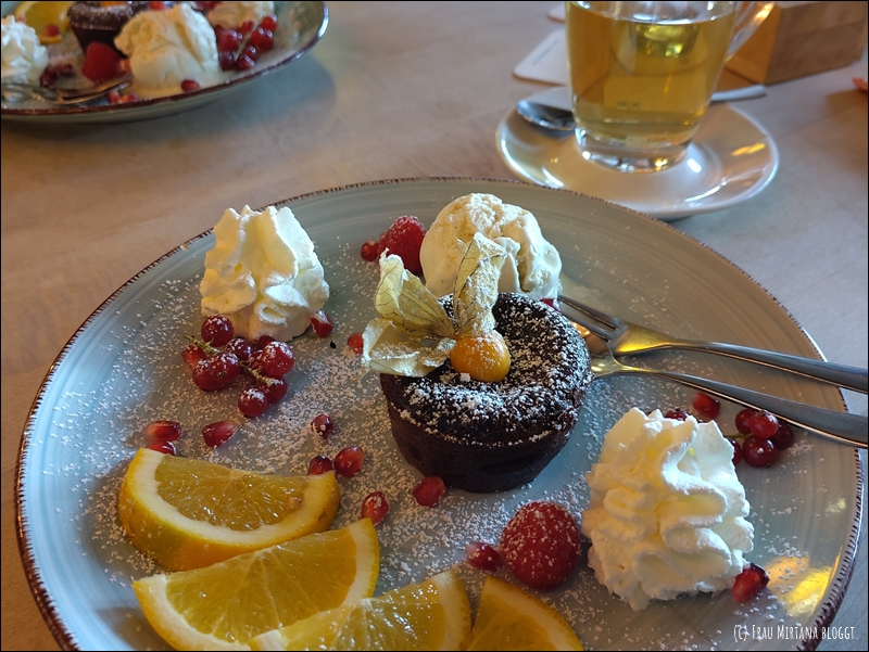 Teller mit einem Schokoküchlein in der Mitte, Orangenscheiben, Sahnetupfer, diverse Beeren, Kugel Vanille-Eis