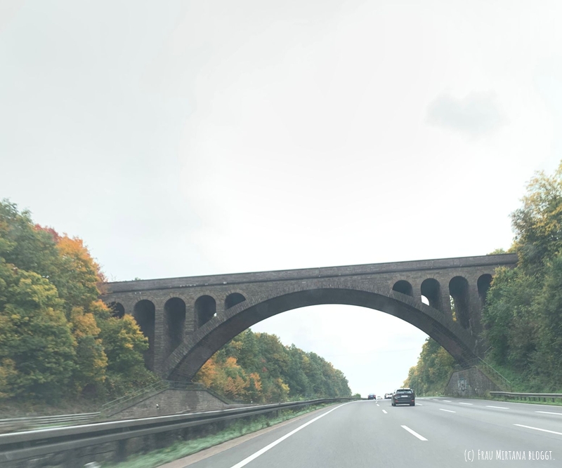 Blick durch die Frontscheibe auf die Autobahn und eine Brücke, grauer Himmel