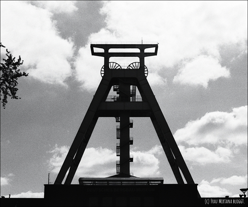 Schwarzweiß, zeigt den Förderturm des Bergbau Museums Bochum vor Wolken am Himmel für Monatsliebe November, kein Bezug zum Text